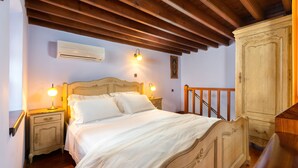 A bedroom with a wooden bed, bedside lamps, a wardrobe, and an air conditioning unit. - Residenza Maria Lindos Villa (Rhodes)