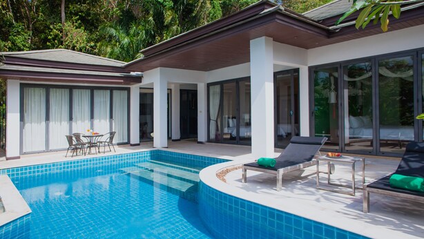 A modern pool area with a clear blue pool, lounge chairs, and a table with chairs. - Baan Eng Fah (Krabi)