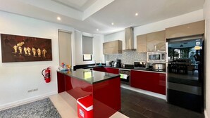A modern kitchen with a central island, stainless steel appliances, and a red accent wall. - Baan Eng Fah (Krabi)