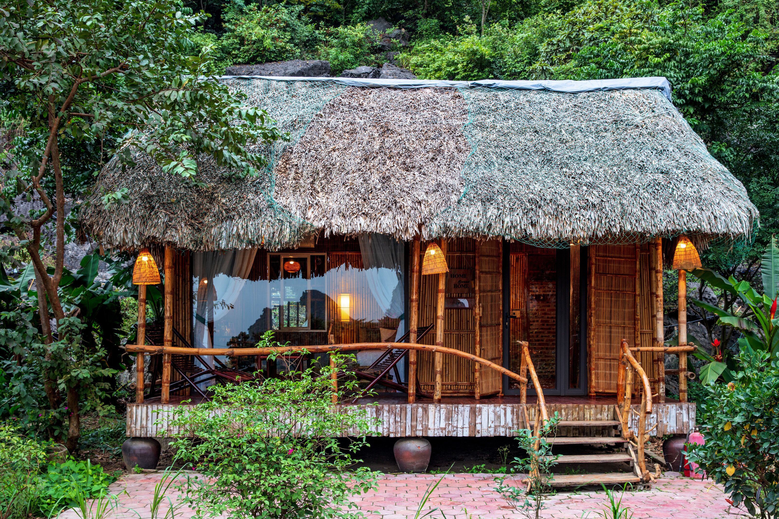A thatched-roof hut with a wooden porch, surrounded by lush greenery.