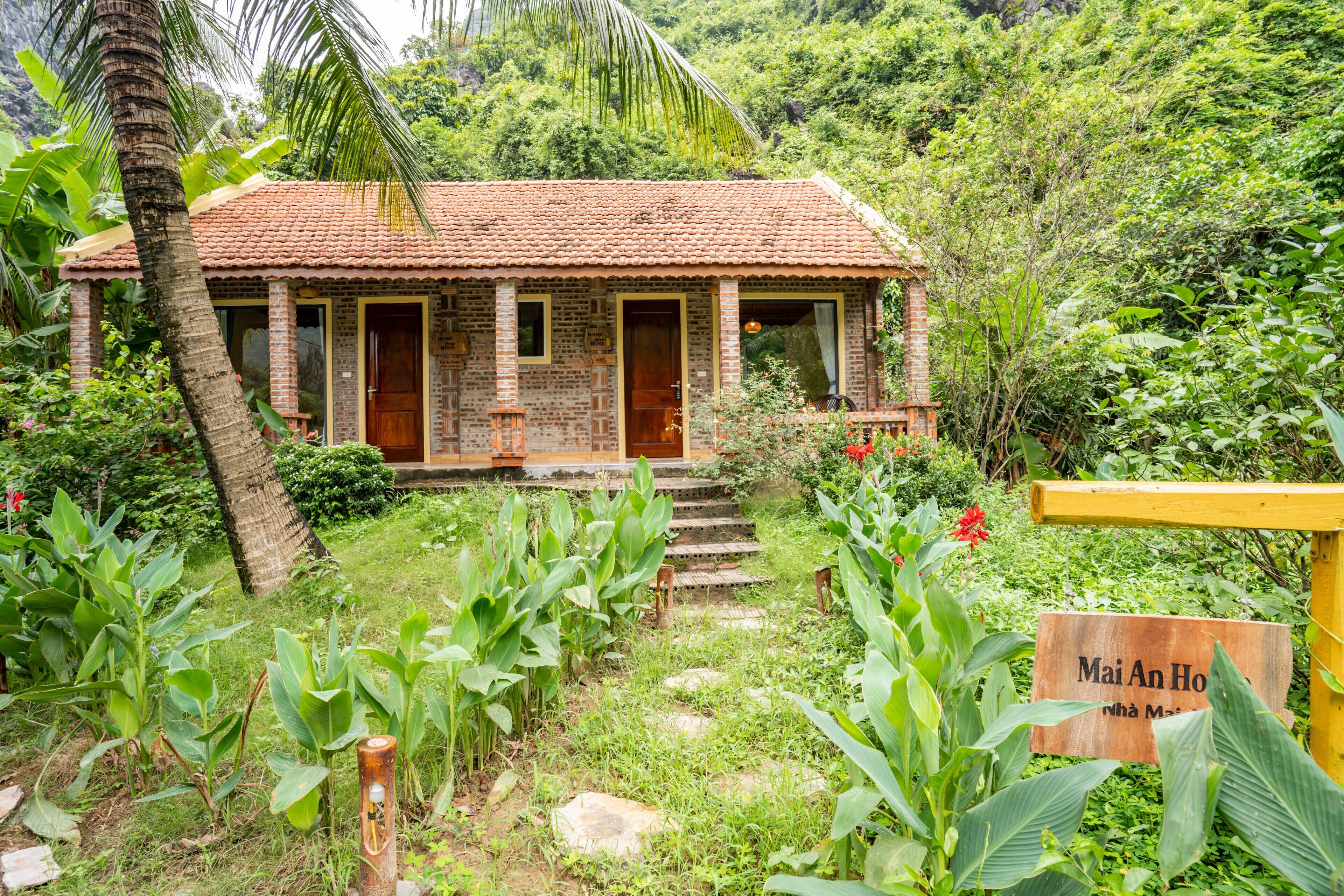 A rustic brick house with a tiled roof, surrounded by lush greenery and a sign reading "Mai An Ho".