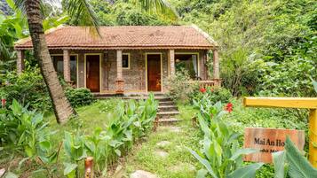 A rustic brick house with a tiled roof, surrounded by lush greenery and a sign reading "Mai An Ho".