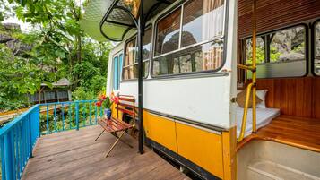 A vintage bus converted into a stationary home with a wooden deck, a bench, and a small garden area.