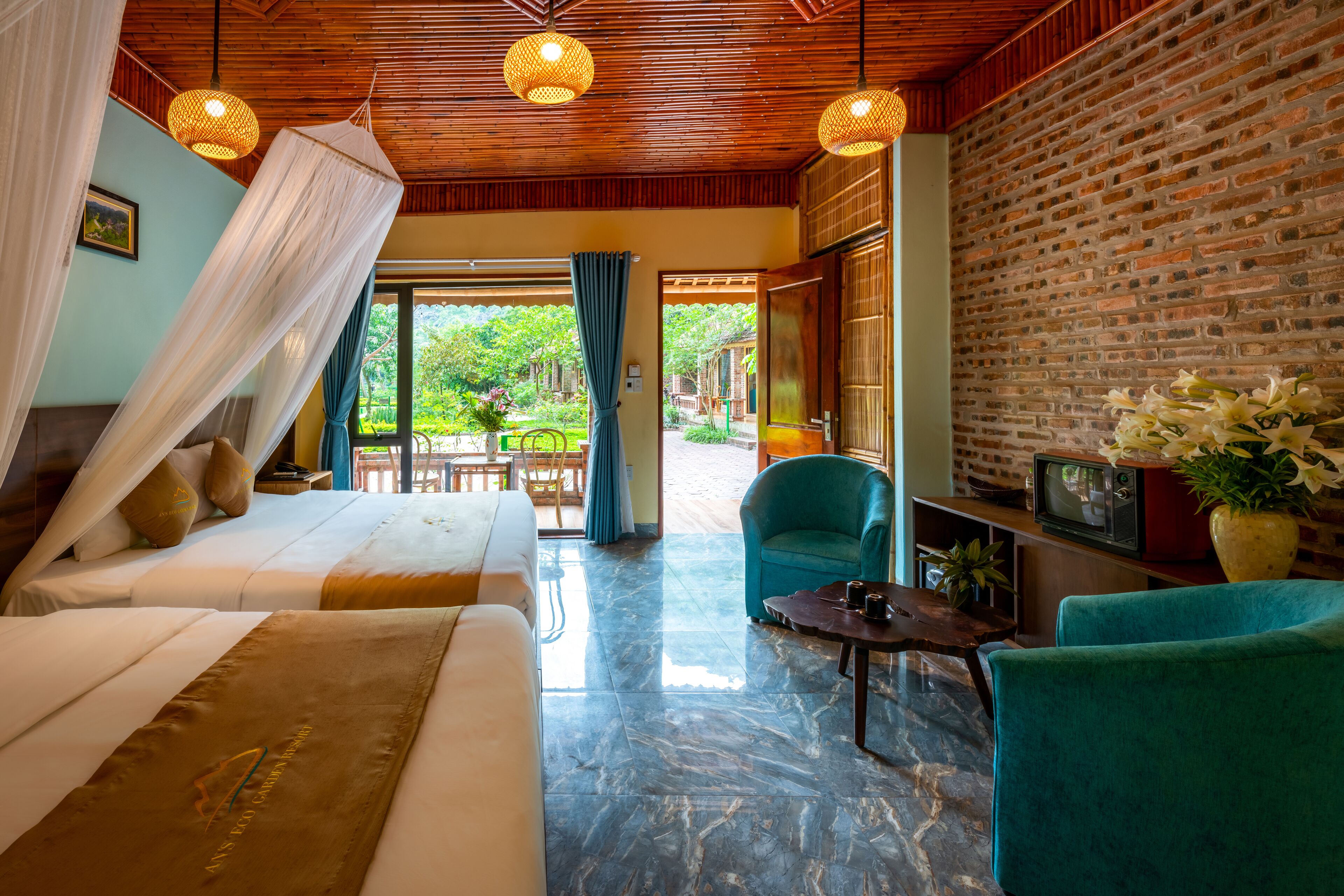 A hotel room with a bed, two chairs, a TV, and a brick wall.