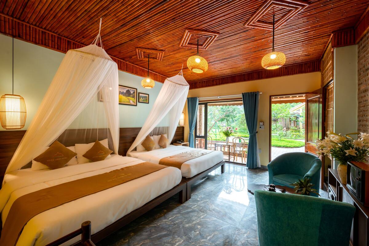 Habitación de hotel con dos camas, techo de madera y vista al jardín.