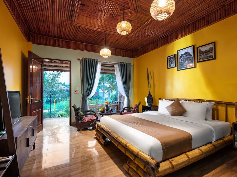 Une chambre dotée d’un grand lit, d’un plafond en bois et offrant une vue sur la verdure environnante.