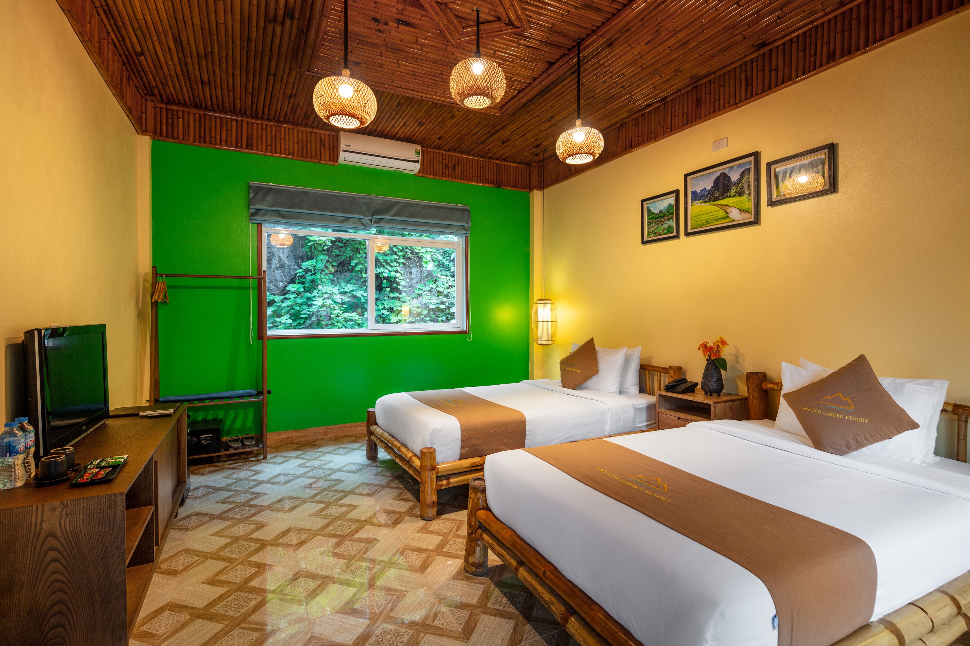 A hotel room with two beds, a TV, a desk, and a window with a view of greenery.