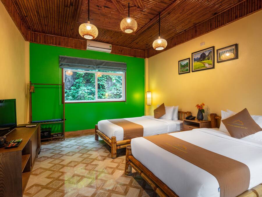 A hotel room with two beds, a TV, a desk, and a window with a view of greenery.