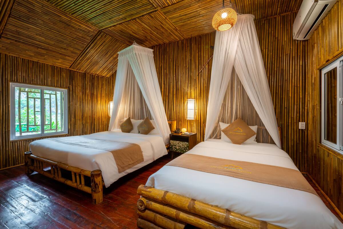 Habitación con dos camas, cada una con dosel, pisos de madera y ventana con vista a la vegetación.