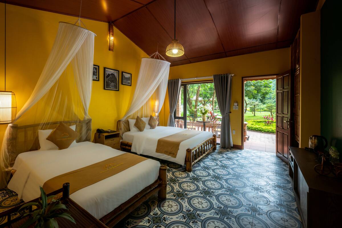 Habitación de hotel con dos camas, un ventanal grande y vistas al jardín.