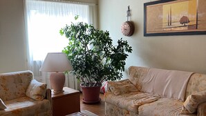 Una sala de estar con dos sofás de estampado floral, una mesa de centro de madera, una planta en maceta, una lámpara y un cuadro enmarcado en la pared.