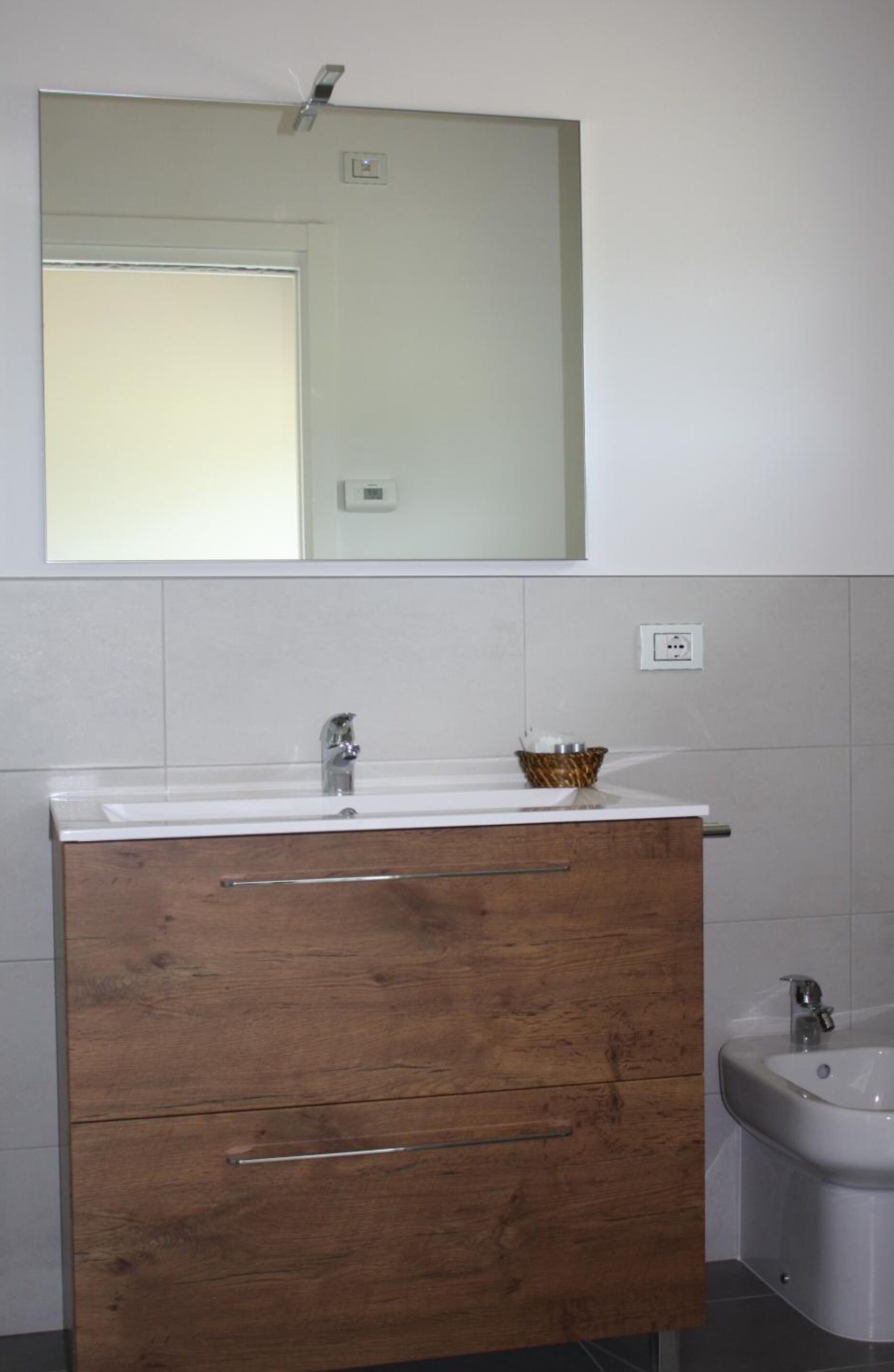 Ein Badezimmer mit einem Holzkosmetikschrank, einem Spiegel über dem Waschbecken und einem separaten Waschbecken auf der rechten Seite.