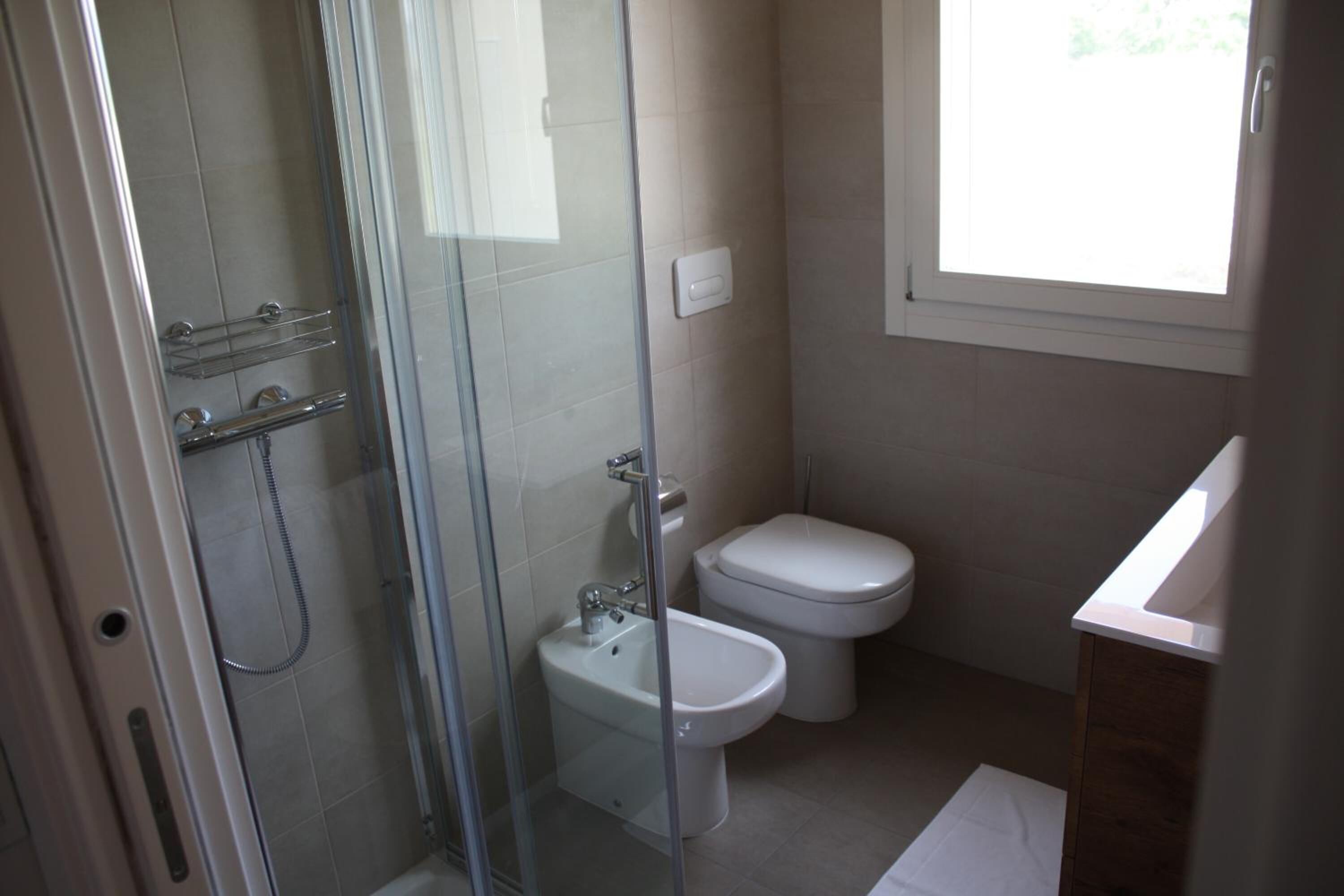 A bathroom with a glass-enclosed shower, a bidet, a toilet, and a sink.