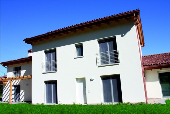 Une maison à deux étages, avec un toit recouvert de tuiles rouges, des murs blancs et un petit balcon.