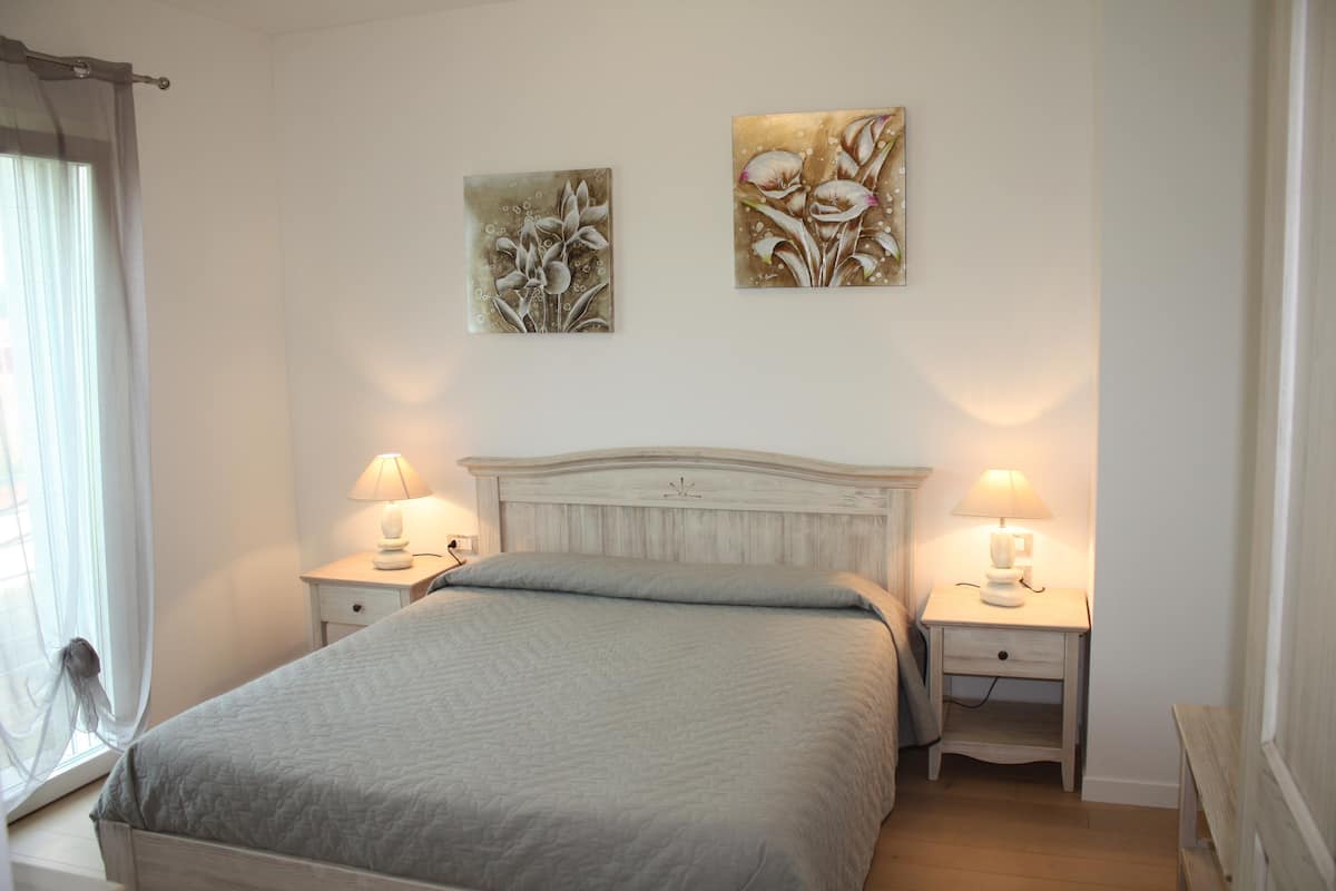 Une chambre à coucher avec un lit, deux tables de chevet avec des lampes et deux tableaux accrochés au mur.