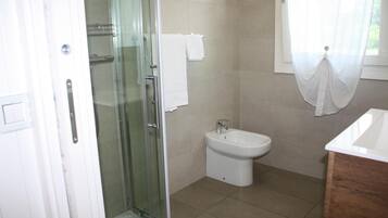 Un baño con cabina de ducha de vidrio, un lavabo blanco y un bidé.