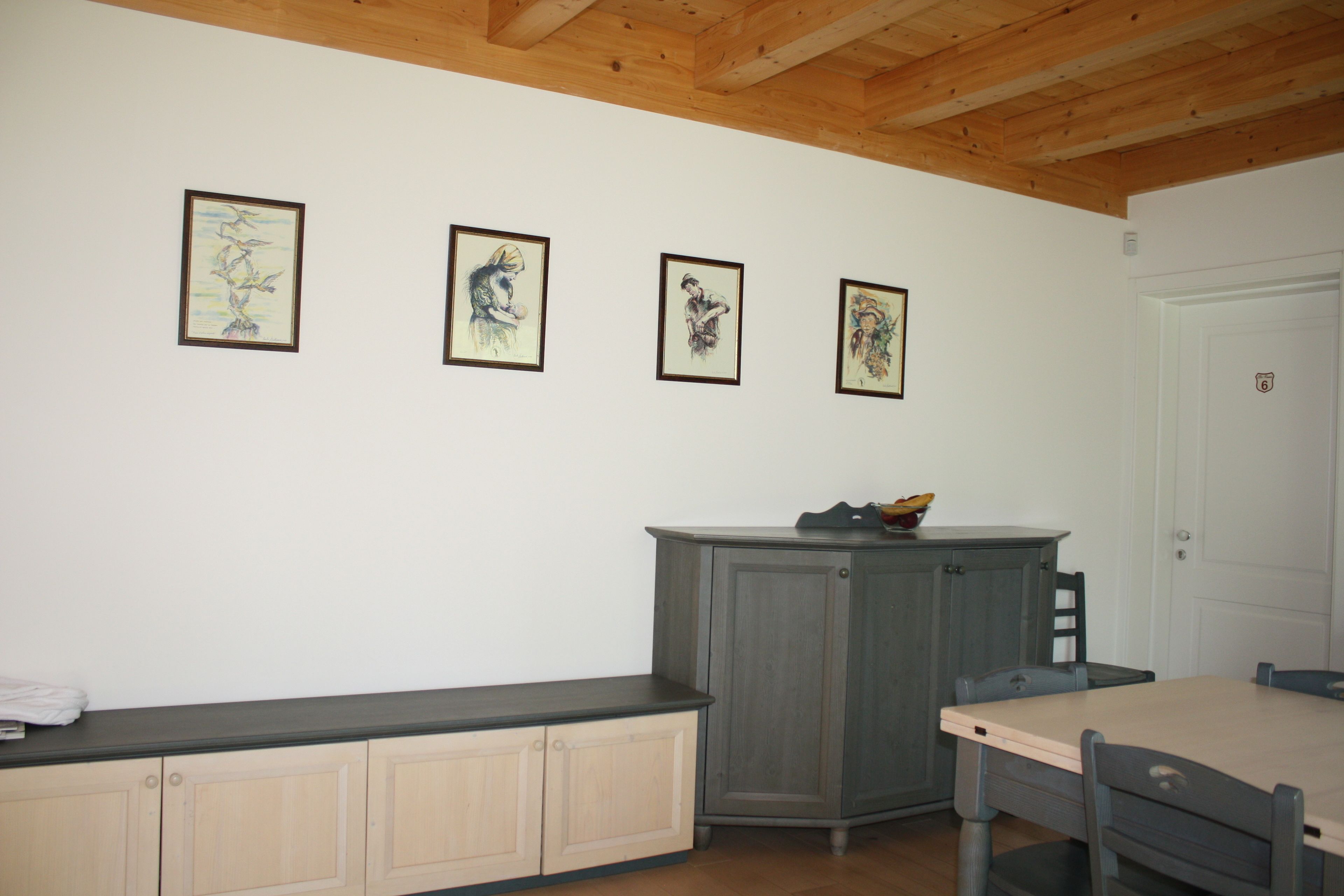 Ein Zimmer mit Holzboden, einem Esstisch, einem grauen Schrank und vier gerahmten Kunstwerken an der Wand.