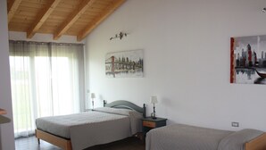 A bedroom with two beds, wooden flooring, a ceiling with exposed beams, a window with sheer curtains, and wall art depicting a cityscape and a boat. - Elis' Rooms (Sernaglia della Battaglia)