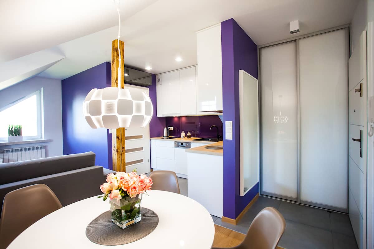 A modern kitchen with white cabinets, a built-in oven, and a dining area with a round table and chairs.