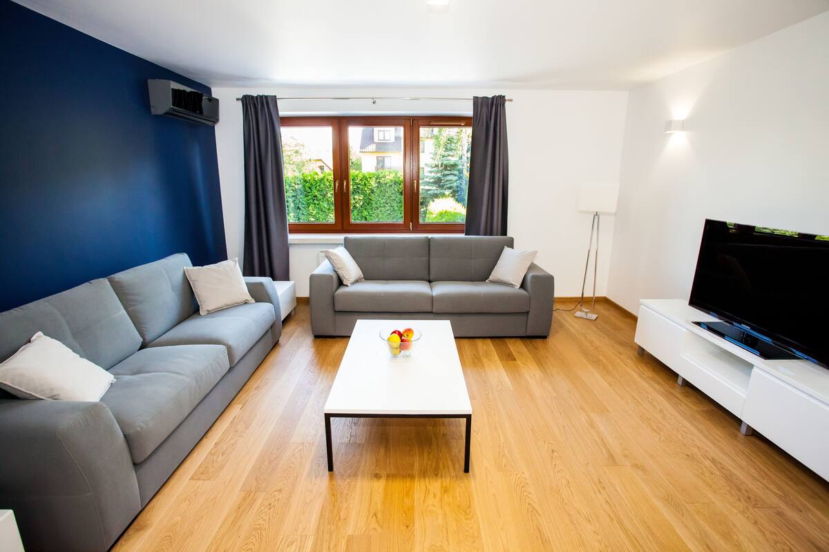 A modern living room with a grey sofa, a white coffee table, and a flat-screen TV on a white stand.