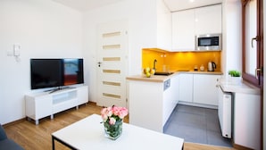 A modern kitchen with white cabinets, a microwave, and a sink. There's a dining table with a vase of flowers. - Apartamenty SaltApart (Wieliczka)