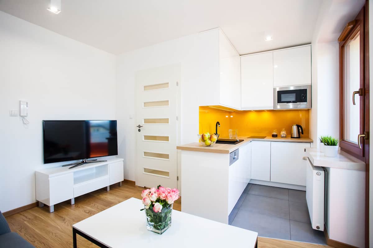 A modern kitchen with white cabinets, a microwave, and a sink. There's a dining table with a vase of flowers.