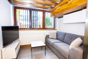 A living room with a sofa, a TV, a small table, and a window with blinds. - Apartamenty SaltApart (Wieliczka)