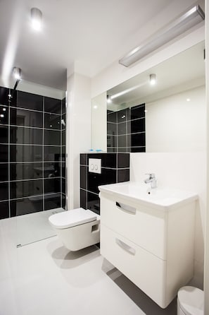 A modern bathroom with a white vanity, a large mirror, and a glass shower enclosure. - Apartamenty SaltApart (Wieliczka)