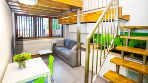 A compact living space with a sofa, dining table, and a staircase leading to a kitchen area. - Apartamenty SaltApart (Wieliczka)
