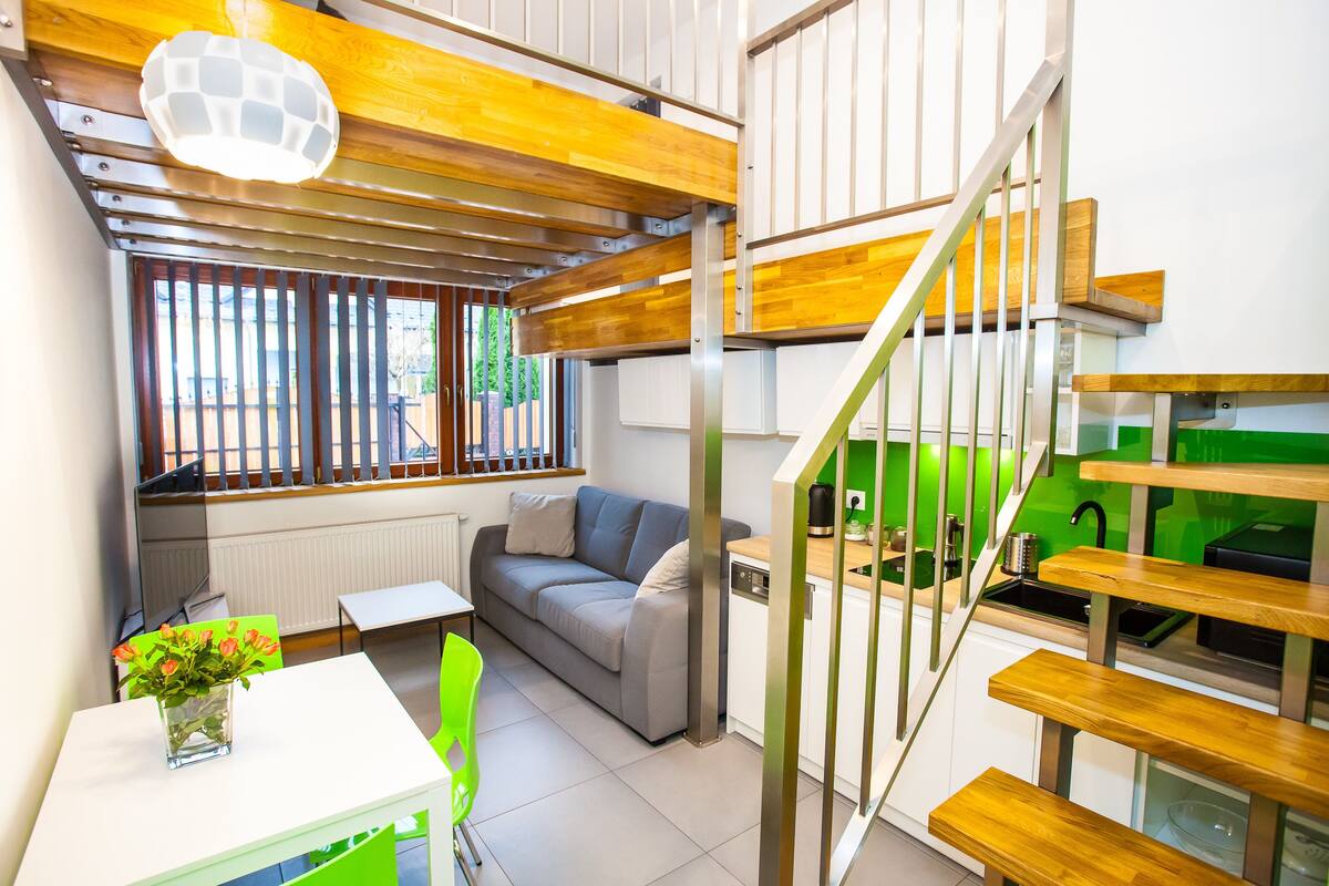 A compact living space with a sofa, dining table, and a staircase leading to a kitchen area.