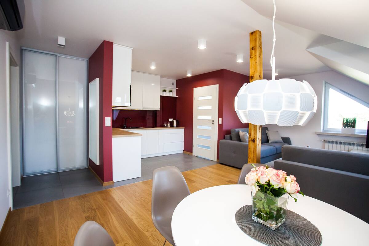 A modern kitchen with white cabinets, a dining area with a round table and chairs, and a living area with a grey sofa.