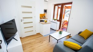 A compact living space with a kitchenette, a sofa with yellow cushions, a coffee table, and a TV on a white cabinet. - Apartamenty SaltApart (Wieliczka)