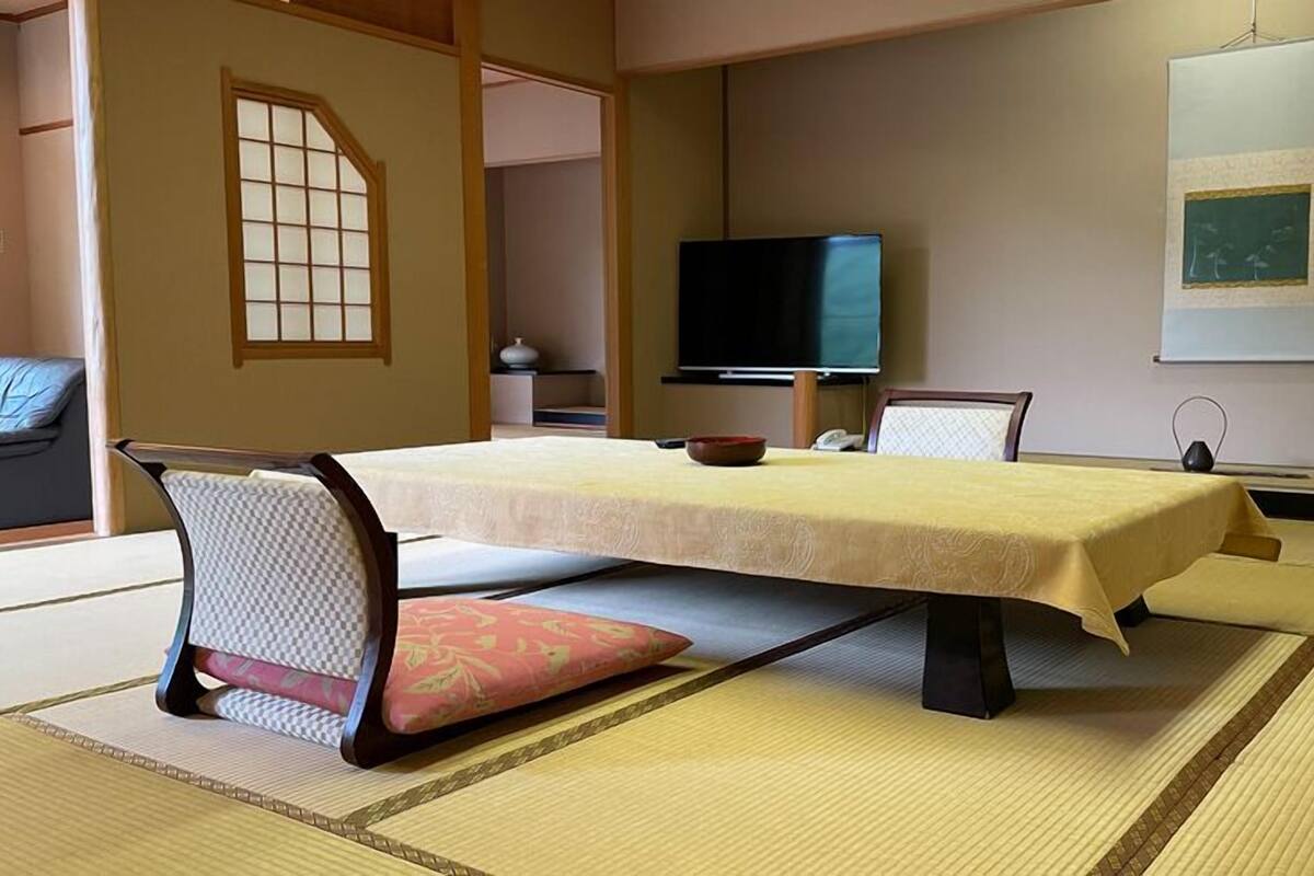 Una habitación con tatami, una mesa baja, sillas, un televisor y un cuadro enmarcado en la pared.