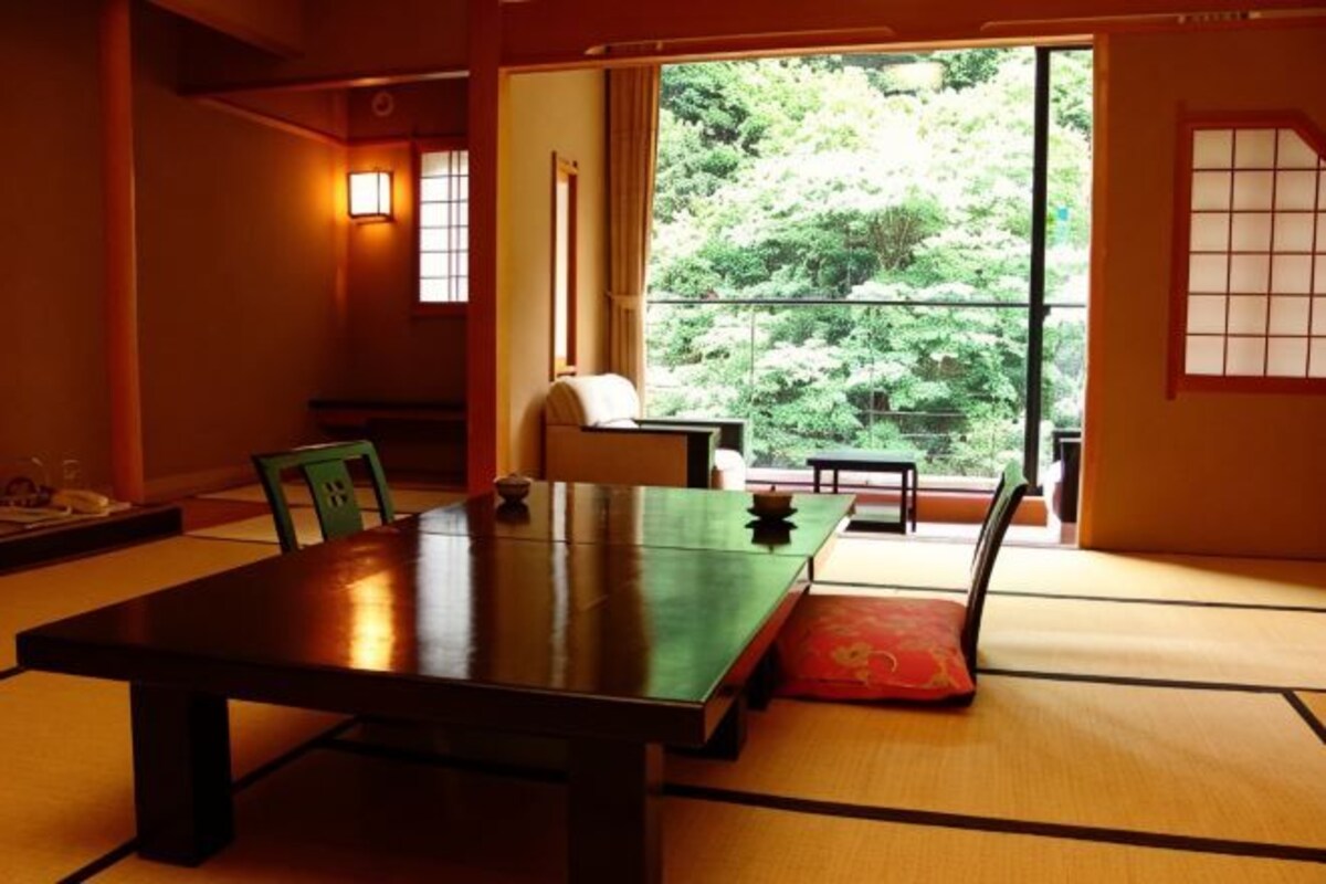 A traditional Japanese room with tatami flooring, a low table, and a view of greenery outside.
