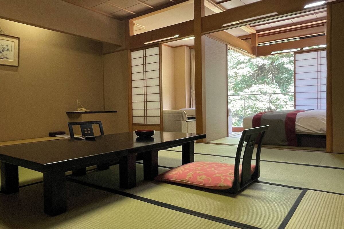 Una habitación tradicional japonesa con suelo de tatami, una mesa baja, una silla con cojín y puertas correderas.
