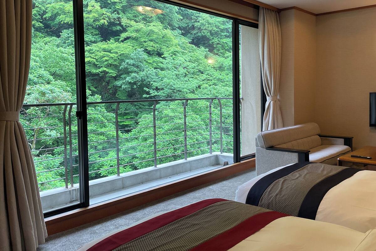 Una habitación de hotel con un ventanal grande, un sofá, un televisor y una mesita.