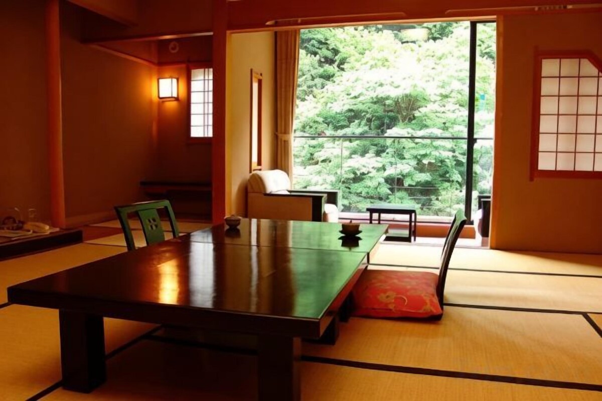 Ein traditioneller japanischer Raum mit Tatami-Boden, einem niedrigen Tisch und Blick auf Grünfläche.