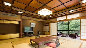 A traditional Japanese room with tatami flooring, a low table, and sliding doors leading to a balcony with a view of trees. - Hotel Ogawa (Asahi)