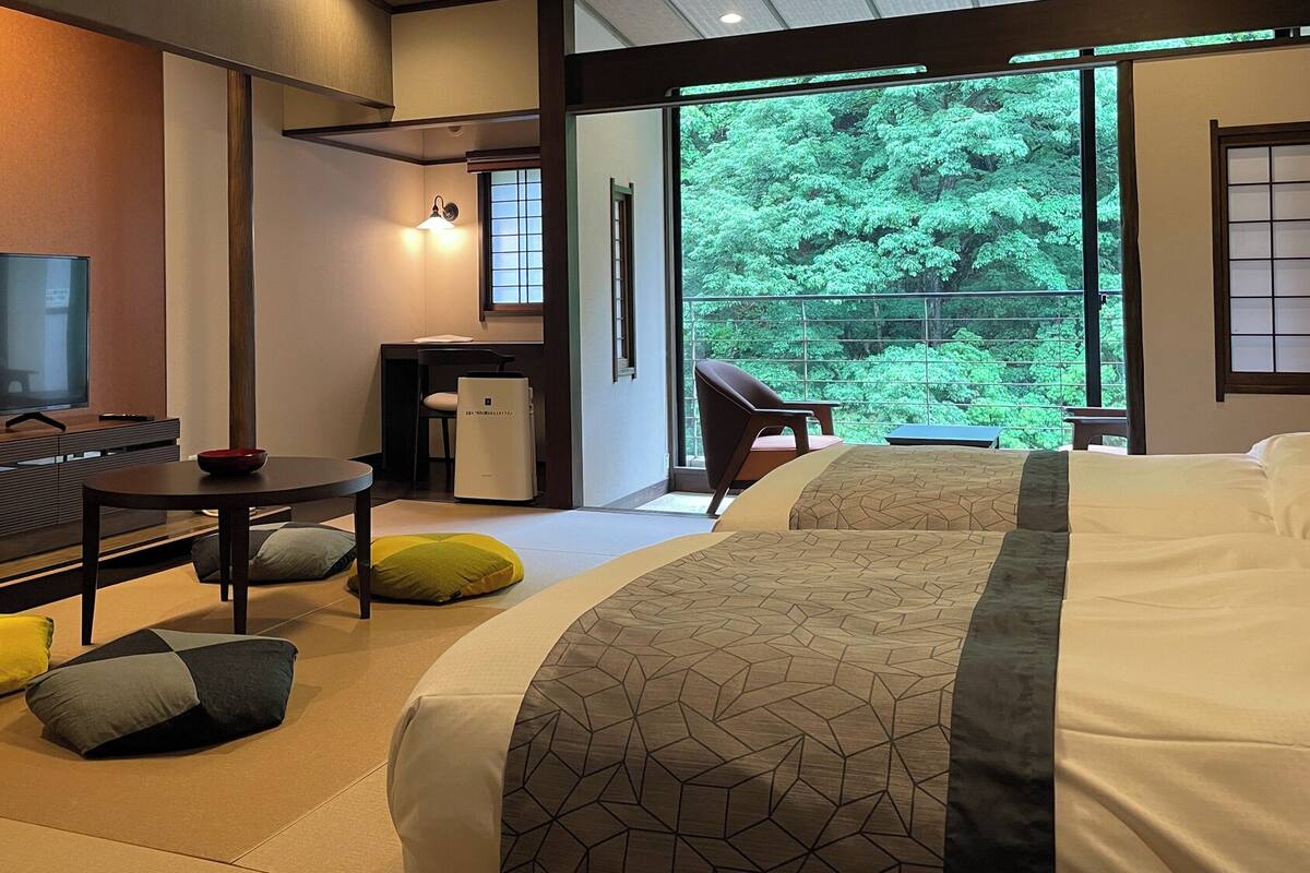 Habitación de hotel moderna con una cama grande, un televisor, un escritorio y vistas al exterior con zonas verdes.