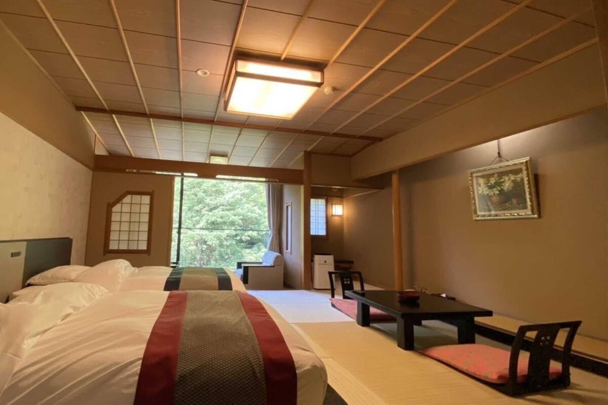 Habitación de hotel con una cama grande, un escritorio, una silla y vistas a árboles por la ventana.