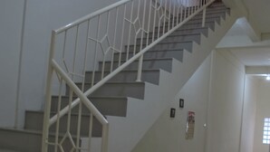 Una escalera con barandillas blancas y escalones grises que lleva a un rellano donde hay una cesta azul en el suelo.