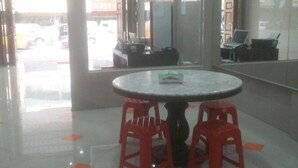 Un vestíbulo amplio con una mesa redonda y taburetes rojos, ventanas grandes y vista a la calle.