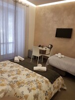 A hotel room with a bed, a desk, a chair, a TV, and a window with curtains.