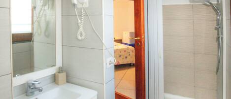 A bathroom with a sink, a hairdryer, and a shower.