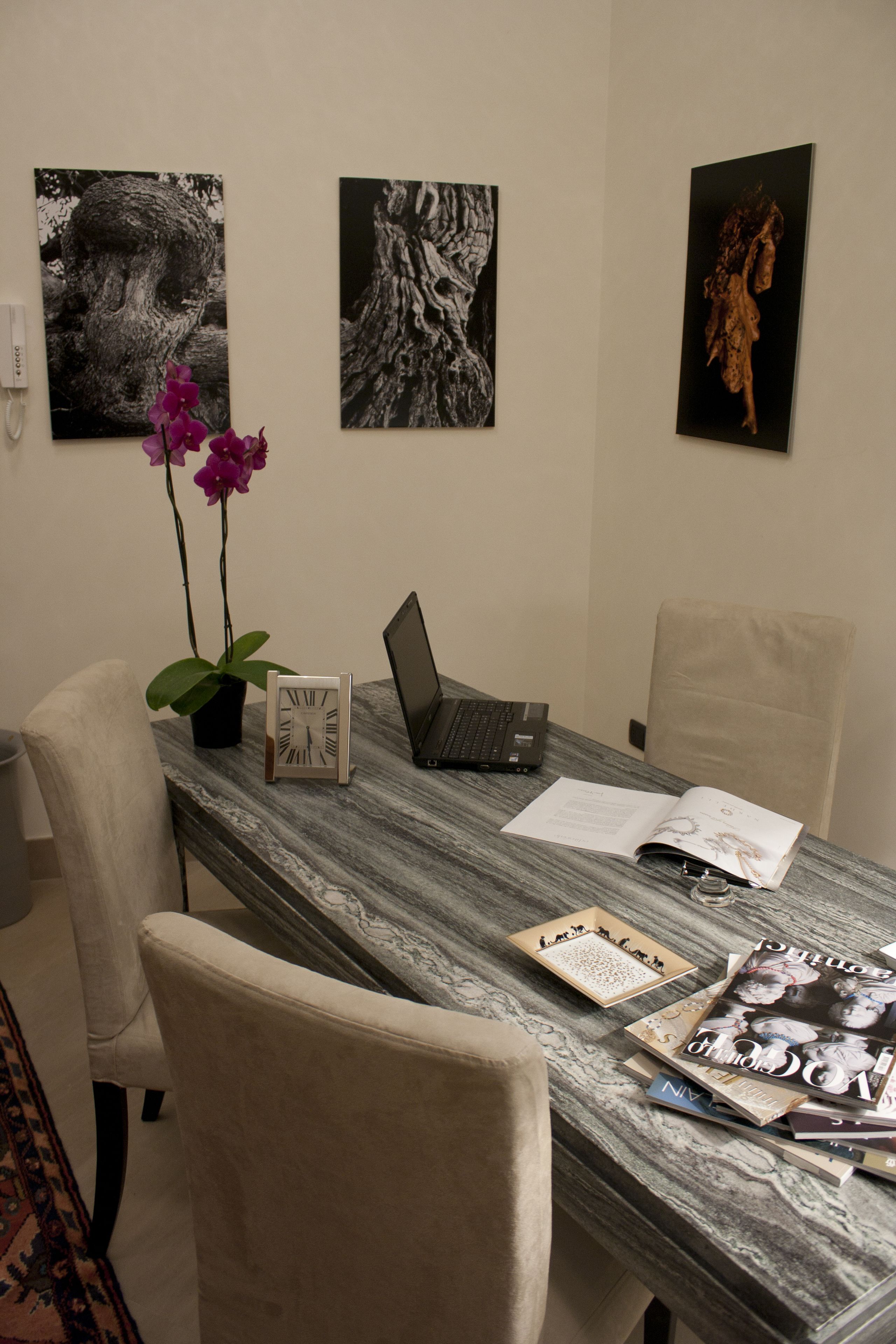 A conference room with a marble table, two chairs, a laptop, a clock, and three framed artworks on the wall.