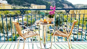A balcony with wicker chairs and a table set with a flower vase, a cup, and a plate of food. - MaLù Bed & Breakfast (Sorrento)