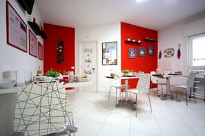 A modern kitchen with white and red decor, a dining area with chairs and a table, and a white cabinet with a geometric design. - MaLù Bed & Breakfast (Sorrento)