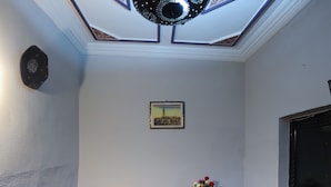 Una habitación de hotel con piso a cuadros, una cama con manta color beige, un techo decorativo y una pequeña mesa con un florero.
