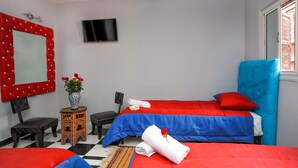 Habitación de hotel con dos camas, un televisor, un espejo y una mesita con flores.