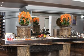 Zona de recepción de un hotel con mostrador de mármol, dos arreglos florales y un espejo que refleja la sala.